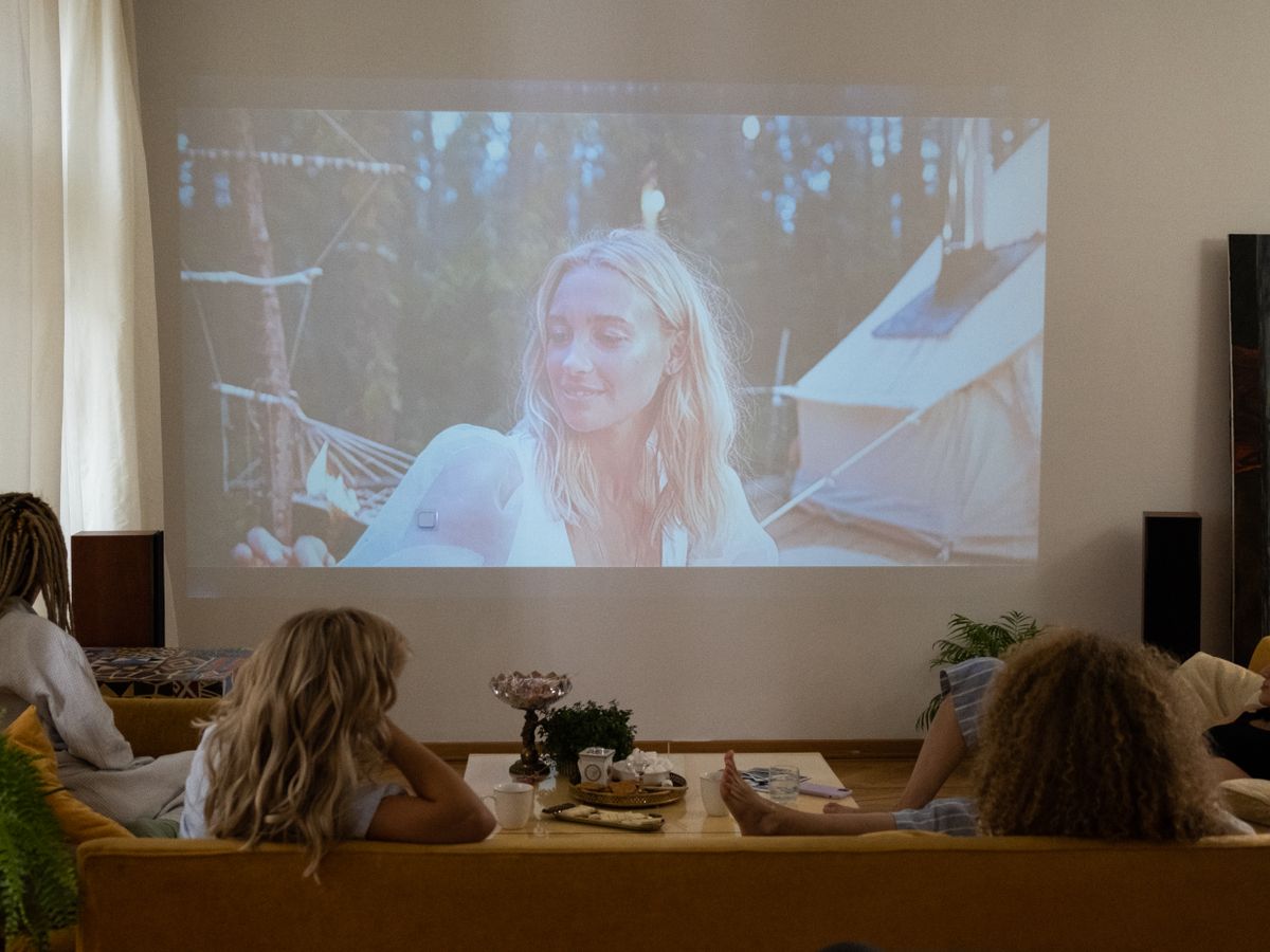 Lidé sledují film promítaný projektorem na stěnu obývacího pokoje